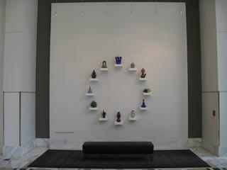 A circular display of ceramic sculptures on small white shelves against a light gray wall.