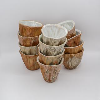 A stack of handmade thrown and altered woodfired ceramic wine cups in earth tones with varying gloss and matte finishes. Photographed against a plain white background.