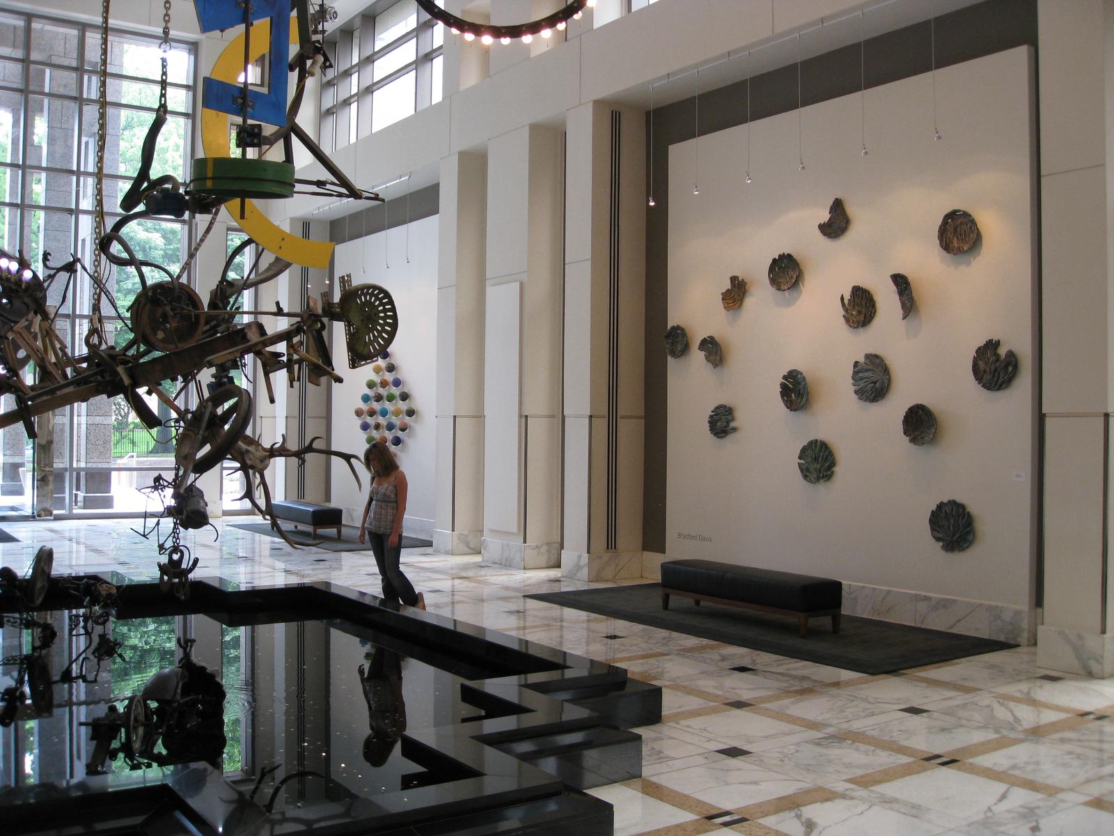 A modern interior with large abstract metal sculpture, reflective black pool, and ceramic wall art.