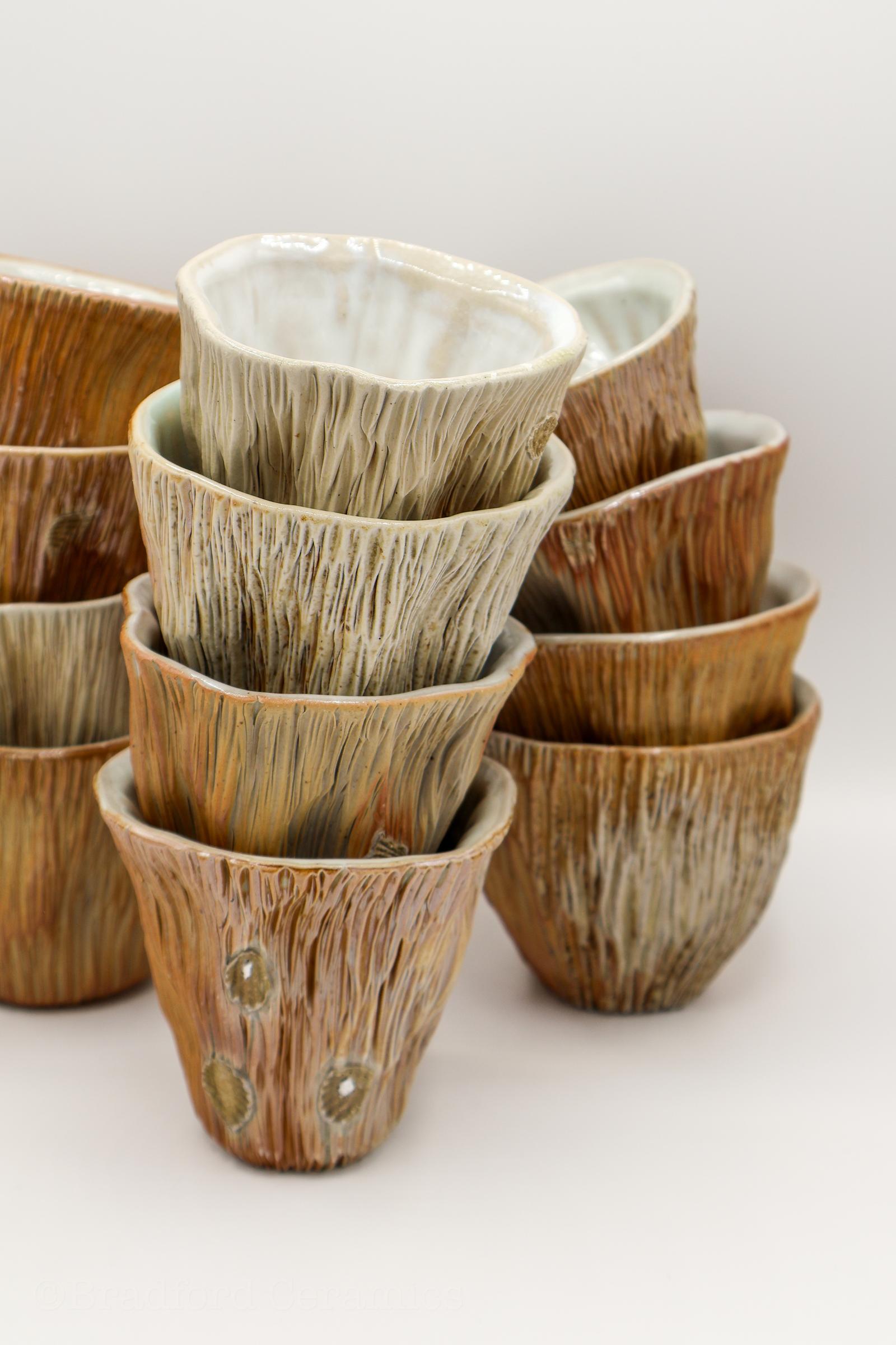 A stack of handmade thrown and altered woodfired ceramic wine cups in earth tones with varying gloss and matte finishes. Photographed against a plain white background.